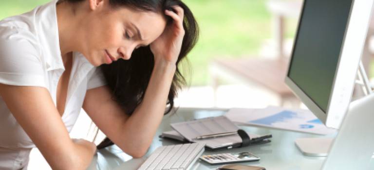 Woman looking stressed at her desk, eyes closed